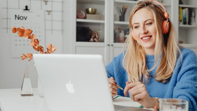 Woman wearing blue sweater and red headphones sitting at desk with laptop and autumn decorations