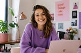 Smiling woman in purple sweater at desk with laptop